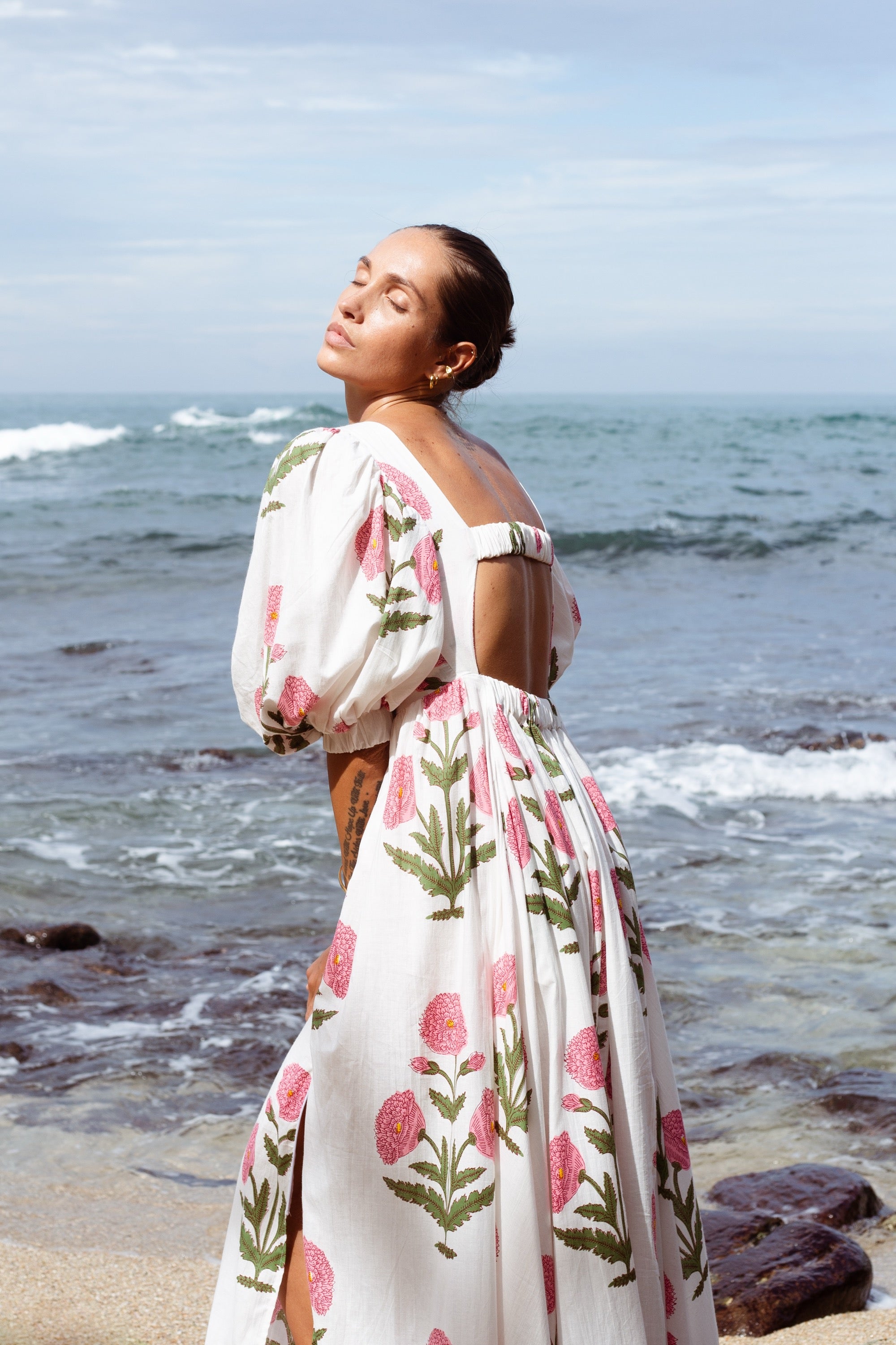 Woman in a floral dress standing on a beach with ocean waves in the background